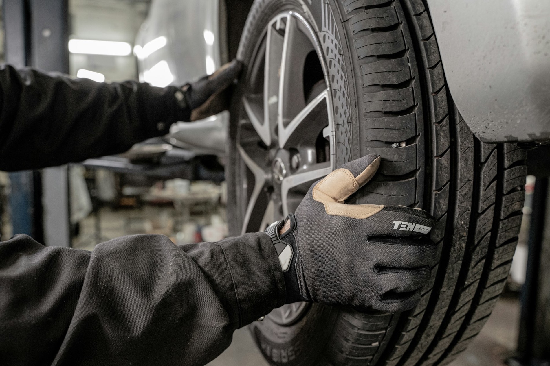 Mains gantées reposant une roue sur un véhicule à l'atelier